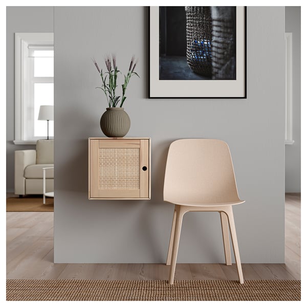 Un espazo de estar moderno cun armario VÄLJARE en tons neutros, cun deseño montado na parede, unha porta tecida e unha cadeira beige.