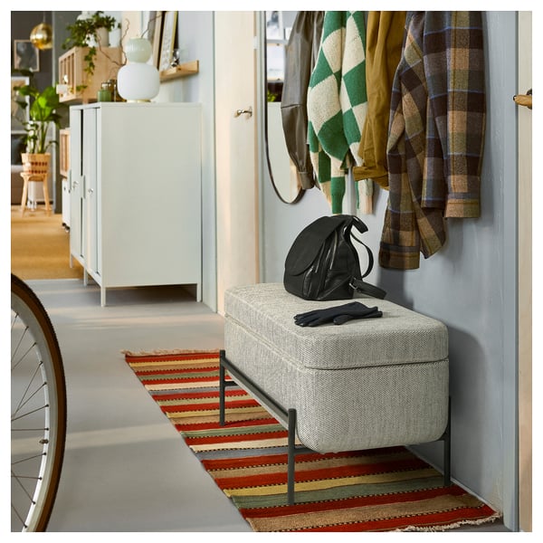 Espazo interior con banco VALTORP, alfombra a raias, mochila, parede azul, chaquetas e unidade de almacenamento.