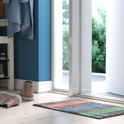 Habitación con parede azul, porta branca, alfombra de raias coloridas, botas rosas.