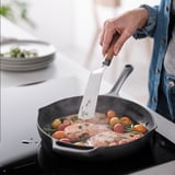 A persoa flipa o peixe cocido con tomates na tixola usando espátula.