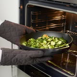 Mans con guantes de forno que sostén a tixola de coles de Bruxelas no forno.
