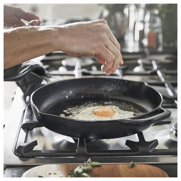 Tixola de ferro fundido negro con dous mangos nunha estufa, aderezada con especias.