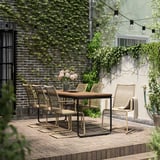 Patio exterior con mesa de madeira e cadeiras de vimbio, rodeado de verde e luces de corda.