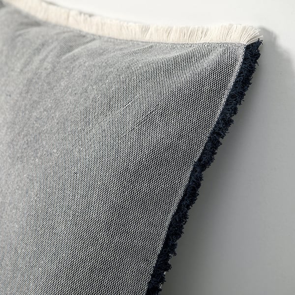 Primeiro plano de cuberta de coxín tecido con bordos de franxas. Tecido gris claro con textura lixeira. As franxas son de cor azul escuro e branco.