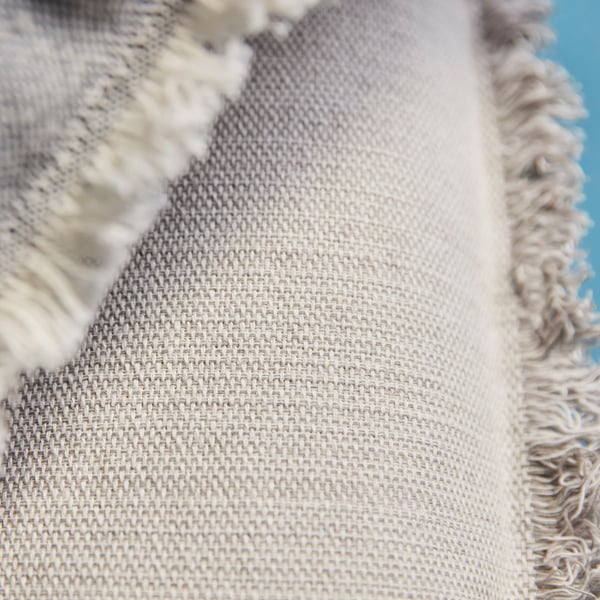 Primeiro plano de tecido beige tecido con fíos visibles e detalles de franxas.