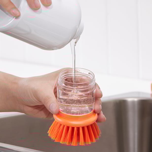 Unha man verte líquido nun frasco transparente de cepillos, demostrando a capacidade de VIDEVECKMAL para almacenar e dispensar líquido de lavado para unha limpeza efectiva.