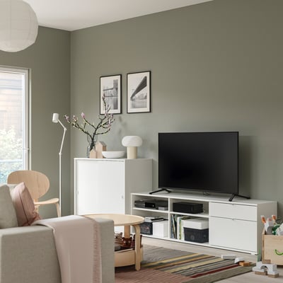 Sala de estar moderna con combinación de almacenamento branco VIHALS, incluíndo un soporte de televisión e armario. Televisión, lámpada e decoración no centro.