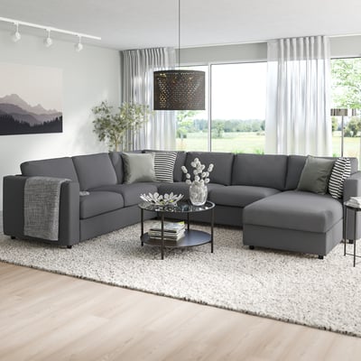 Moderno gris en forma de L VIMLE sectional nunha sala de estar luminosa, con coxíns suaves e unha elegante mesa de café escura.