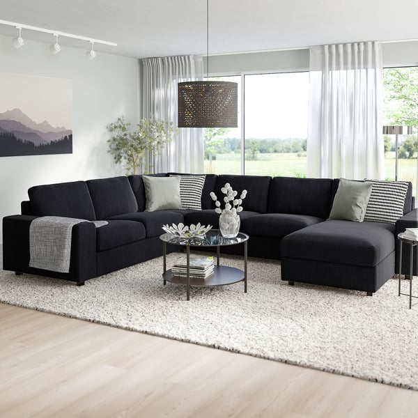 Unha sala de estar moderna cun sofá seccional negro VIMLE, mesa de café, alfombra e coxíns.