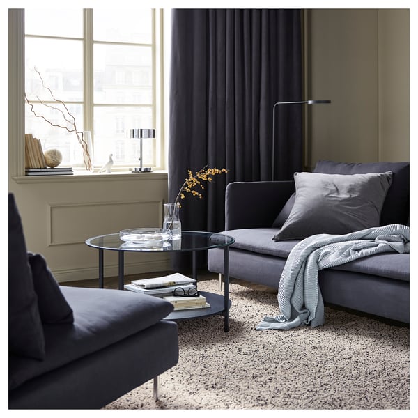 Sala de estar moderna con alfombra VINDUM gris, sofá gris, mesa de café de vidro preto da fiestra, vaso decorativo e lámpada.