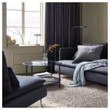 Sala de estar moderna con alfombra VINDUM gris, sofá gris, mesa de café de vidro preto da fiestra, vaso decorativo e lámpada.