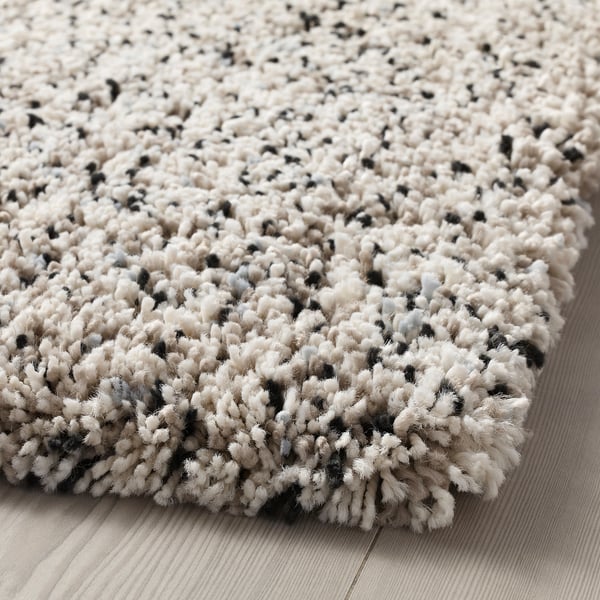 Alfombra grosa e de peluche con manchas negras, colocada sobre chan de madeira. Textura suave e invitante.