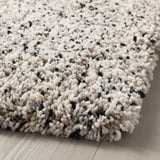 Alfombra grosa e de peluche con manchas negras, colocada sobre chan de madeira. Textura suave e invitante.