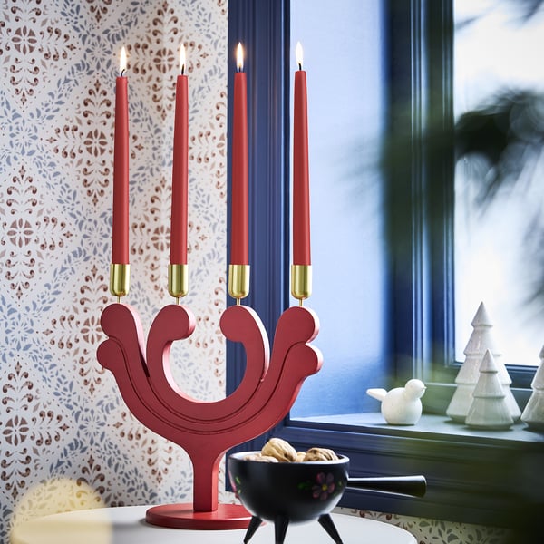 Portavelas vermello VINTERFINT con acentos dourados e velas acesas, xunto ás galletas e decoracións de Nadal, contra unha parede con patróns.