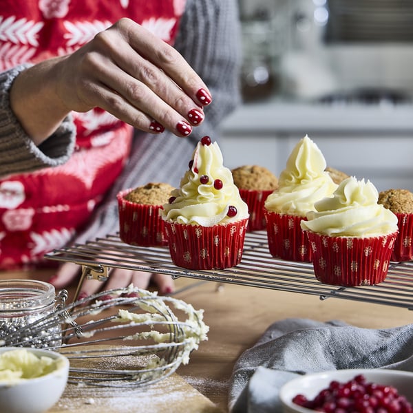 Unha persoa decora cupcakes en cuncas de forno vermellas festivas con xeado e bagas.