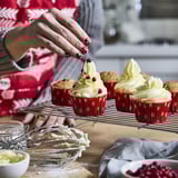 Unha persoa decora cupcakes en cuncas de forno vermellas festivas con xeado e bagas.