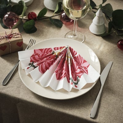 Unha mesa con pratos brancos e pratería. Servilletas coloridas e dobradas sentan enriba de cada prato. Vasos de viño e decoracións de vacacións rodean o escenario.