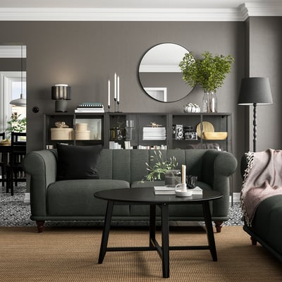 Sala de estar moderna con sofá VISKAFORS gris, mesa de café negra, alfombra gris e libraría escura con elementos de decoración.