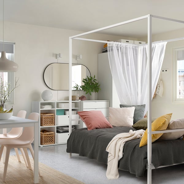 Unha cama VITARNA con cortinas, roupa de cama gris e almofadas de cores nun dormitorio pequeno e elegante. Ten almacenamento debaixo.