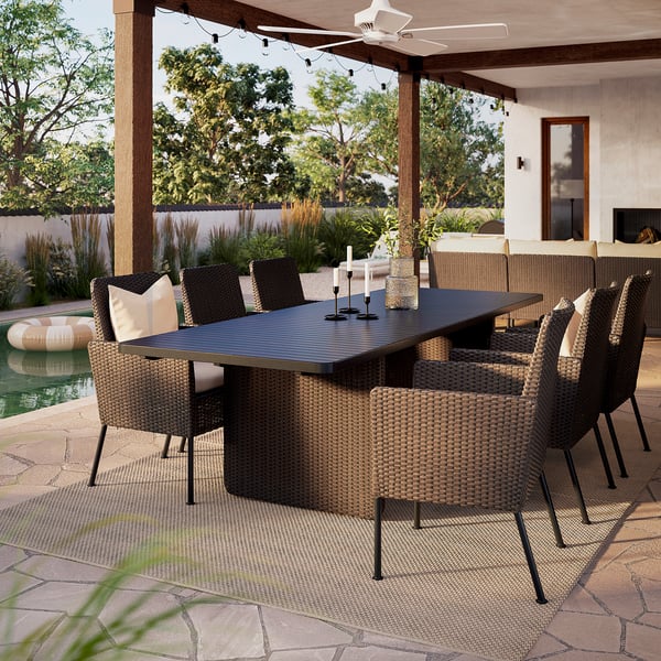 Patio exterior con mesa rectangular VITTSKÄR e cadeiras de vimbio, situado baixo unha pérgola, rodeado de verde e piscina.