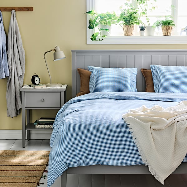 Xogo de edredón azul e branco sobre cama feita, lámpada, libros, plantas.