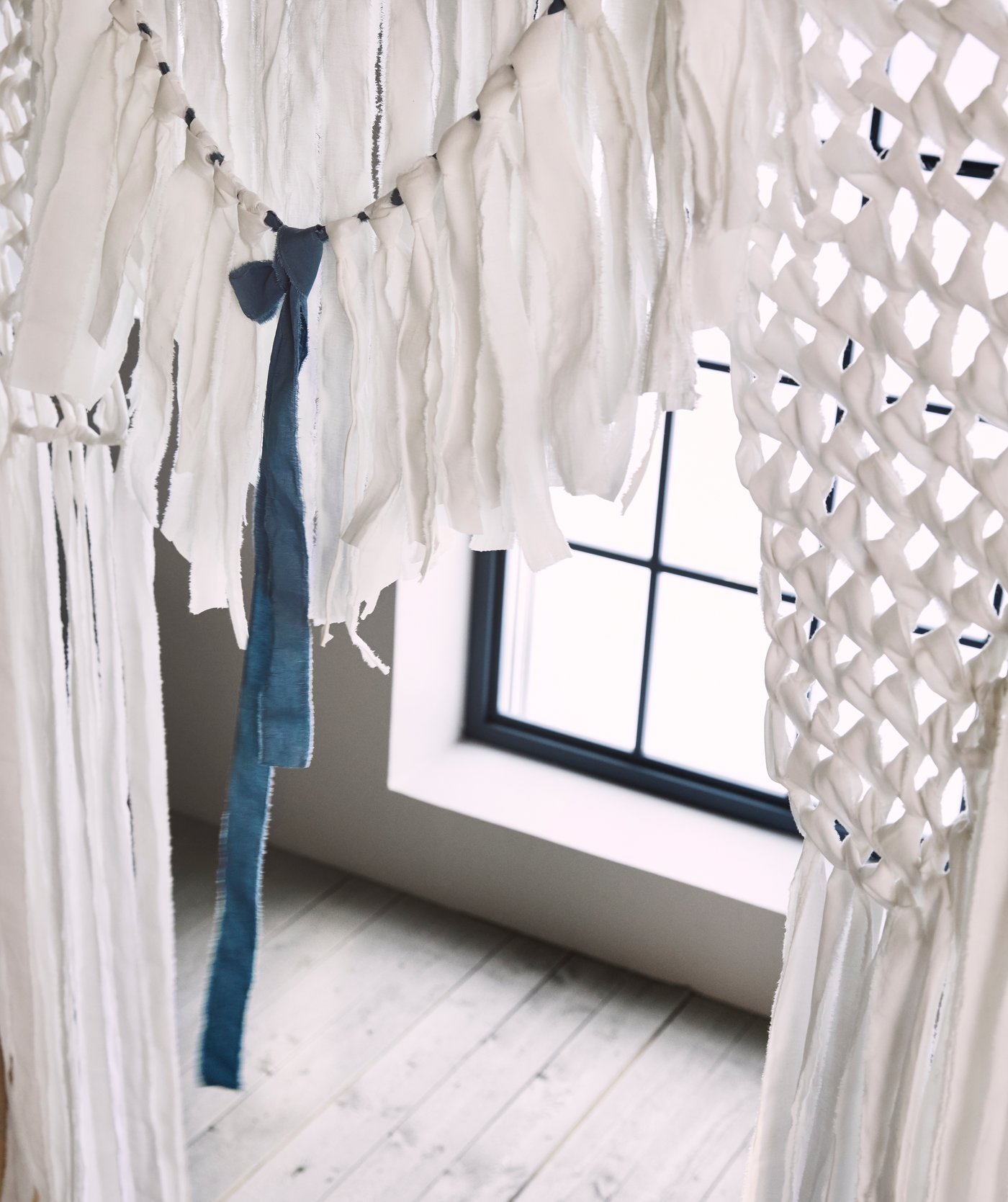 Part of a wedding arbor made from white and blue cotton strips tied together to produce a rustic lace effect.