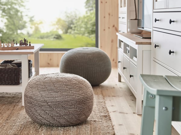 Nahaufnahme von zwei runden Pouffes as Stoff, die auf einem Juteteppich vor einem weissen Couchtisch aus Holz stehen