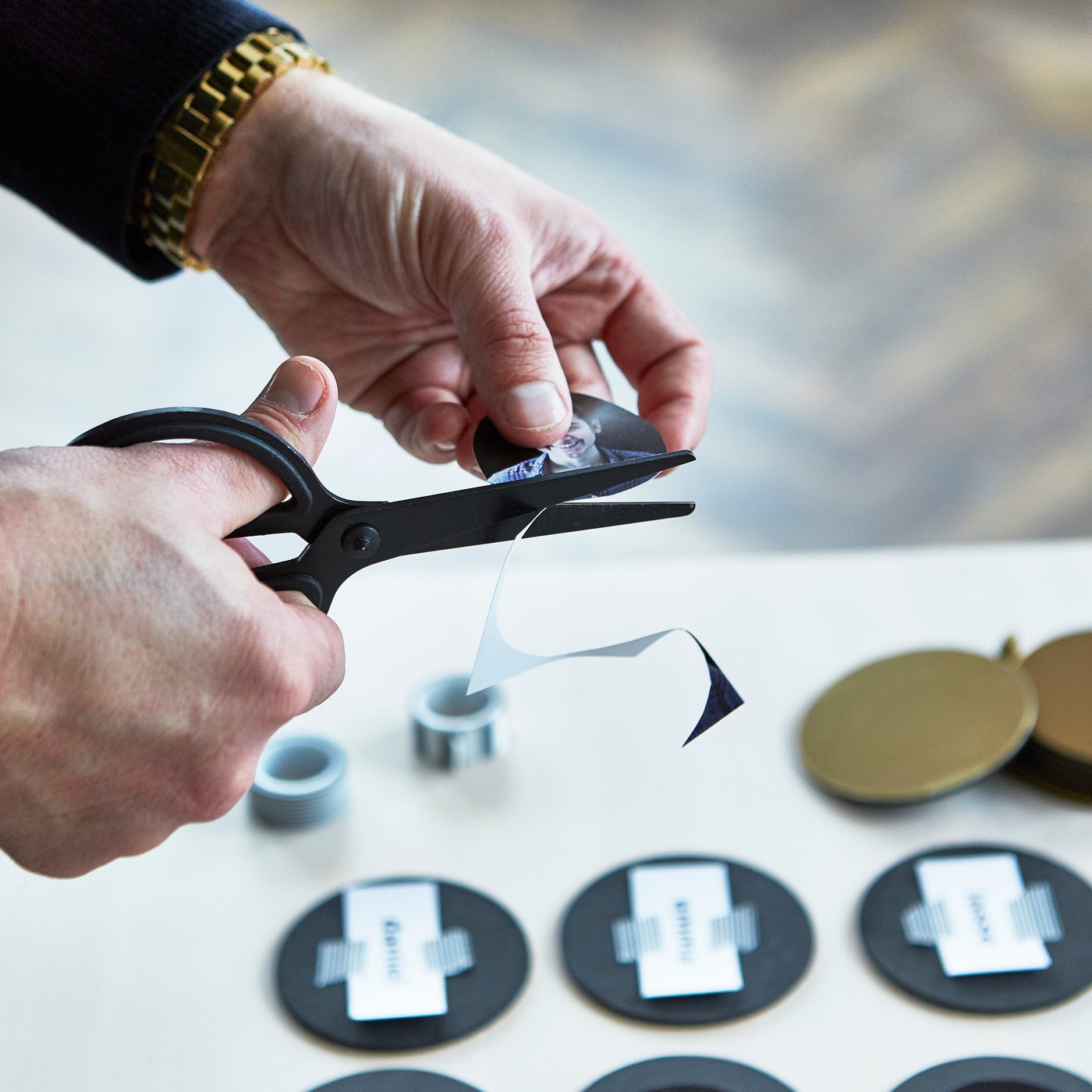 Someone cuts out photos with a black FULLFÖLJA pair of scissors and turns gold-coloured GLATTIS coasters into their own memory game.