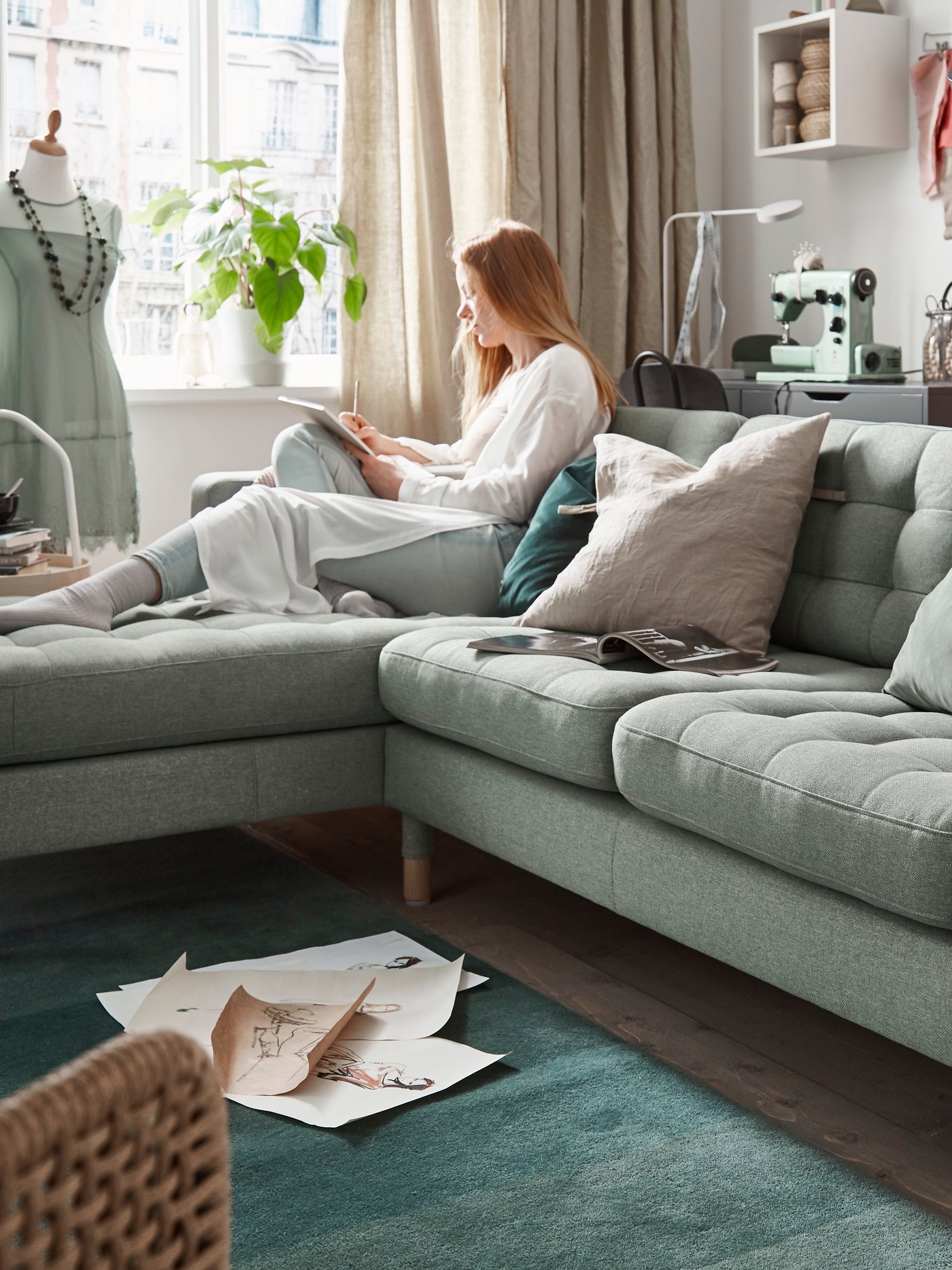 A woman is sitting on a light green LANDSKRONA sofa with chaise longue in the living room.