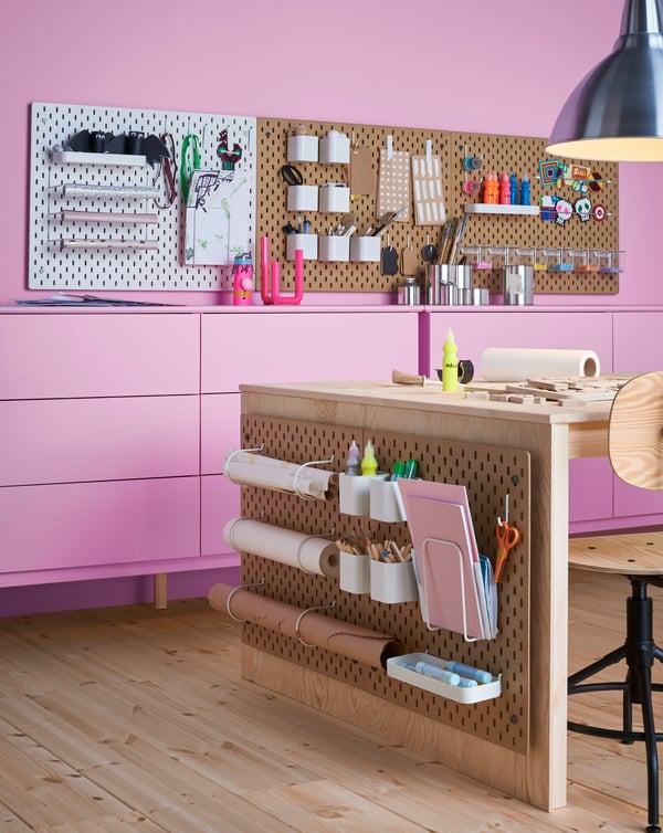 Mehrere SKÅDIS Lochplatte aus Holz an der Wand in einem Hobbyzimmer, daran zu sehen Zubehör, Papier und mehr.