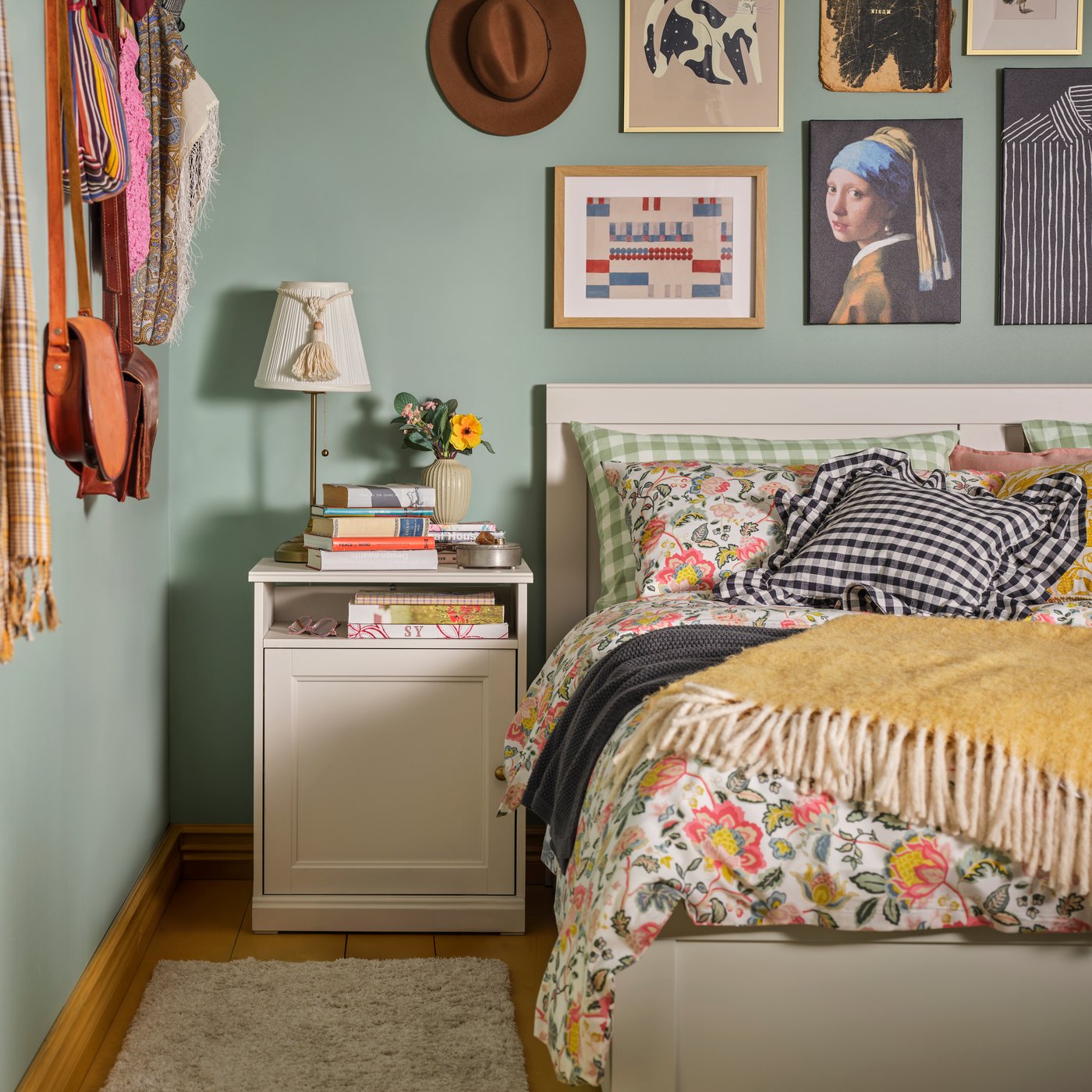 A bedroom with an off-white FÅGELFJÄLLET bedside table beside a FÅGELFJÄLLET bed frame, adorned with floral bedding.