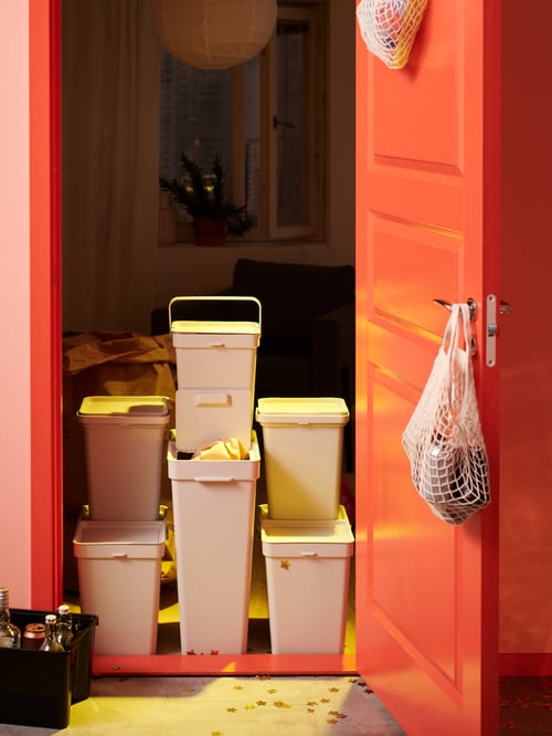 View of room entrance, orange door, bins with lids, in various sizes, placed on top of each other, net bags on door handle.