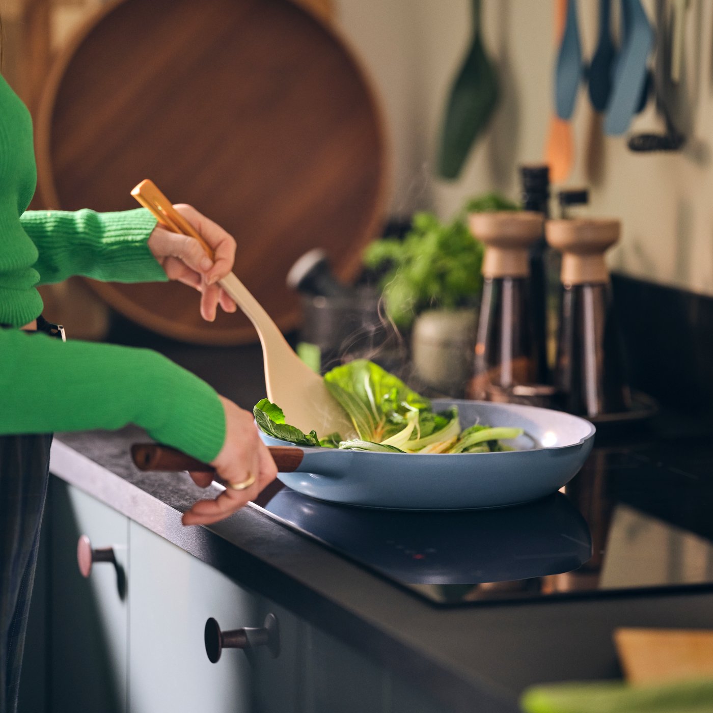 Un donna sta cucinando in una cucina con ante frontali per cassetto KALLARP verde-grigio scuro lucido