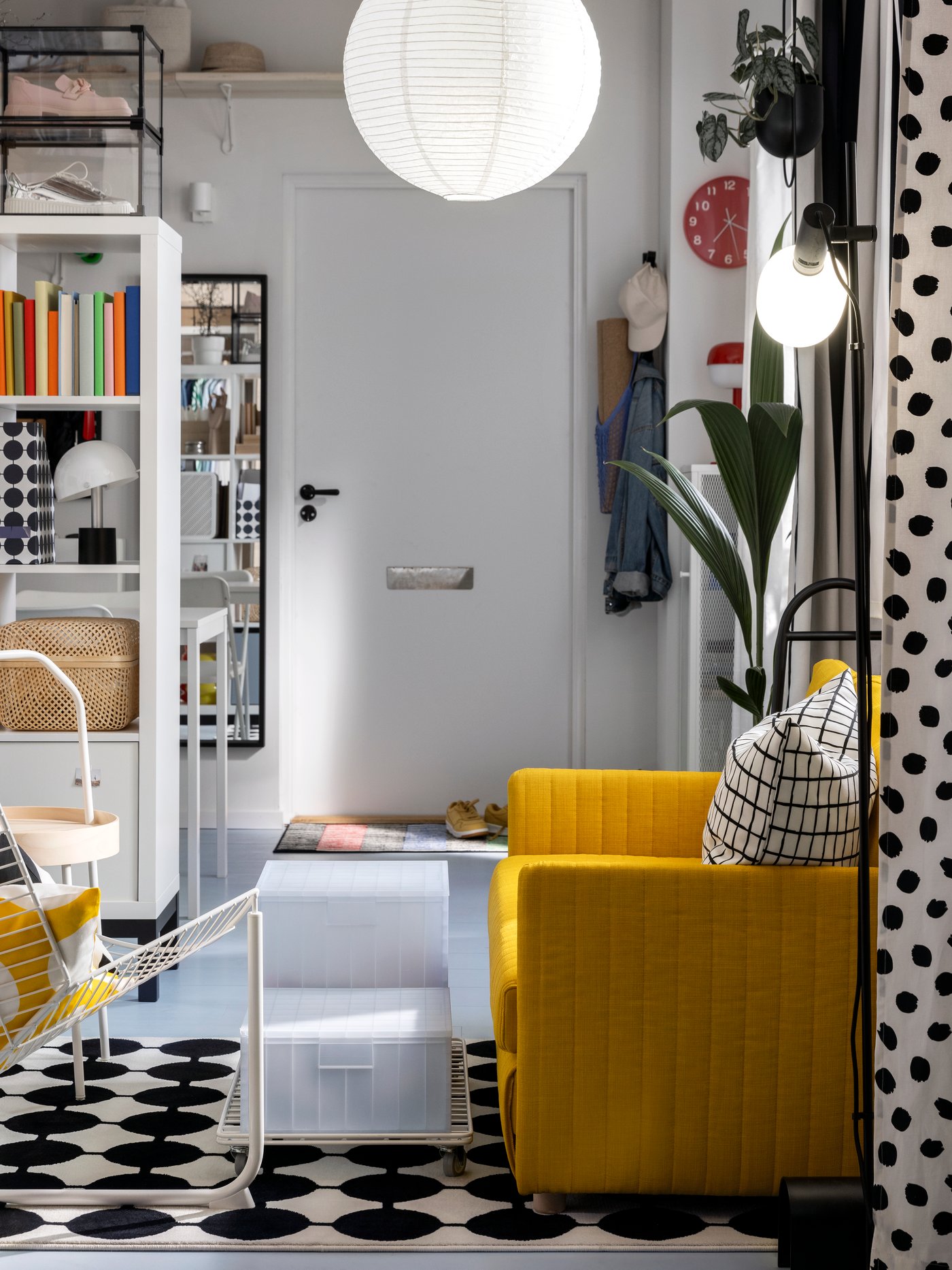 Několik úložných krabic PANSARTAX s víkem přistavených na vozíku INVALLNING ke žluté rozkládací pohovce FRIDHULT.