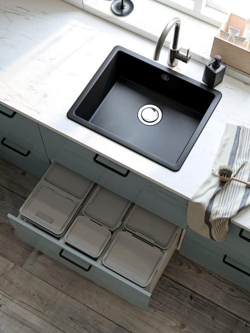Top view of kitchen with black quartz composite rectangular sink, pewter tap, and open drawer underneath holding bins.
