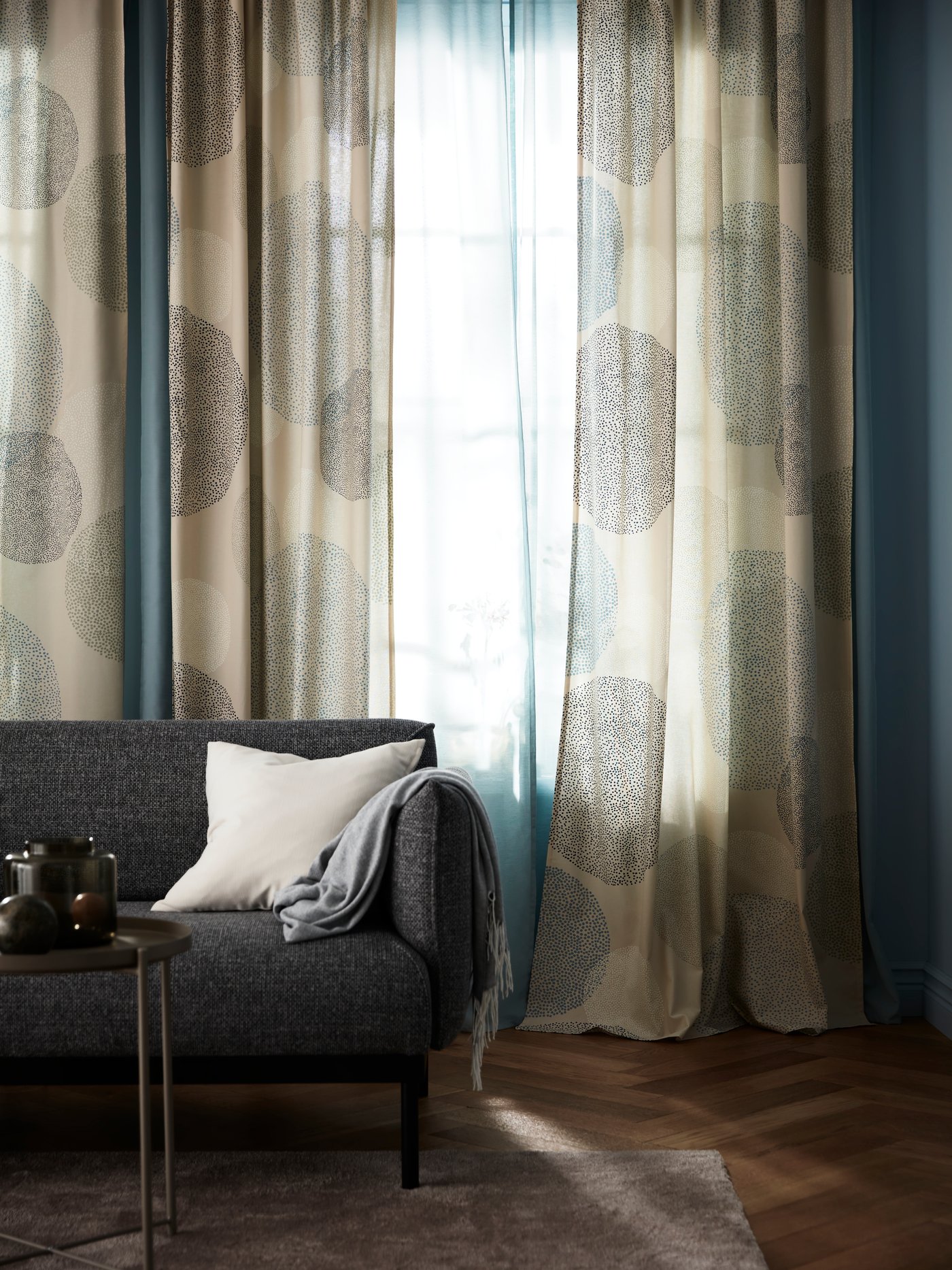 Ett vardagsrum med en mörl soffa och ljusa, skira gardiner.