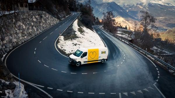 Un veicolo elettrico per le consegne IKEA in movimento lungo una tortuosa strada di montagna in Svizzera.