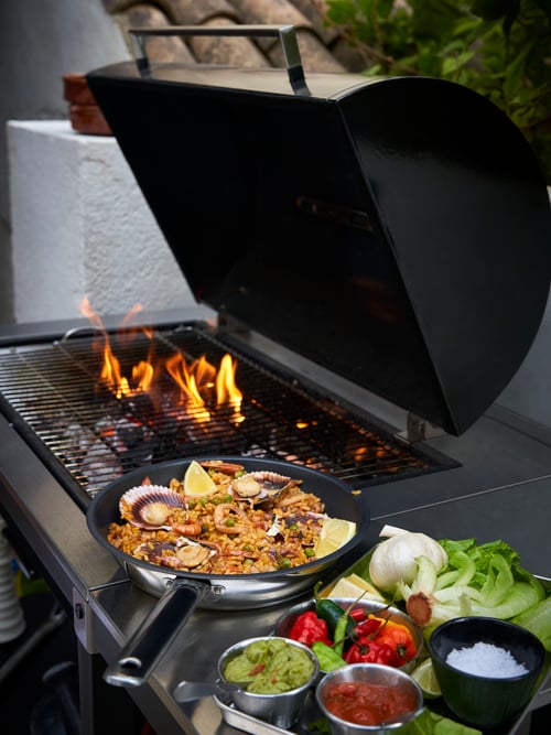 În aer liber, cu un grătar cu cărbuni gri GRILLSKÄR cu masă laterală, o tigaie IKEA 365+ și o tavă de servire GRILLTIDER.