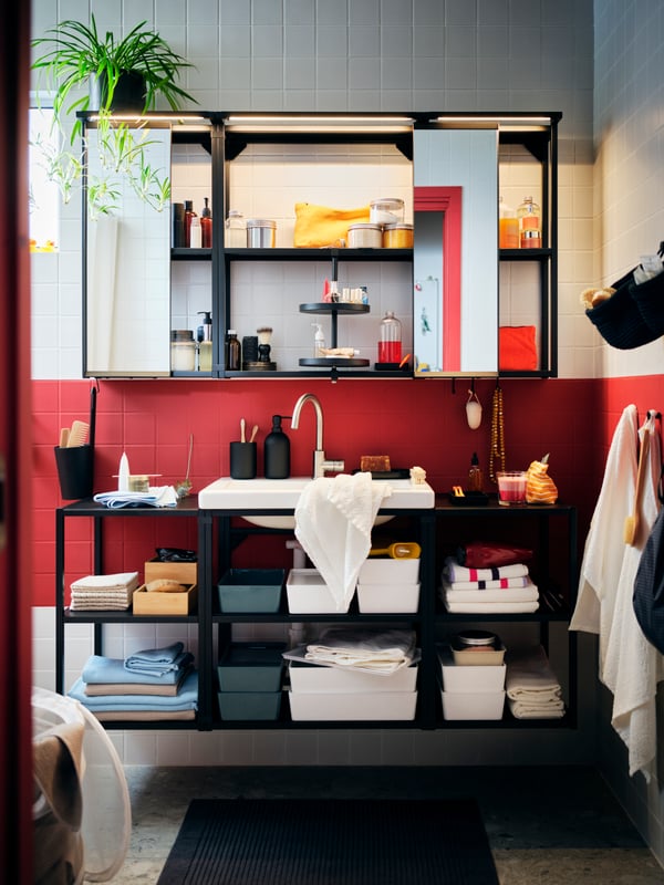A red-and-white-tiled bathroom with a big ENHET combination with open cabinets, filled with neatly arranged accessories.