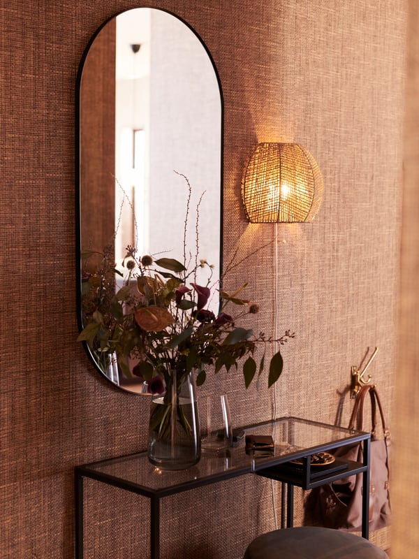A handmade sedge MÅNALG wall lamp next to a black LINDBYN mirror above a black-brown/glass VITTSJÖ laptop table.