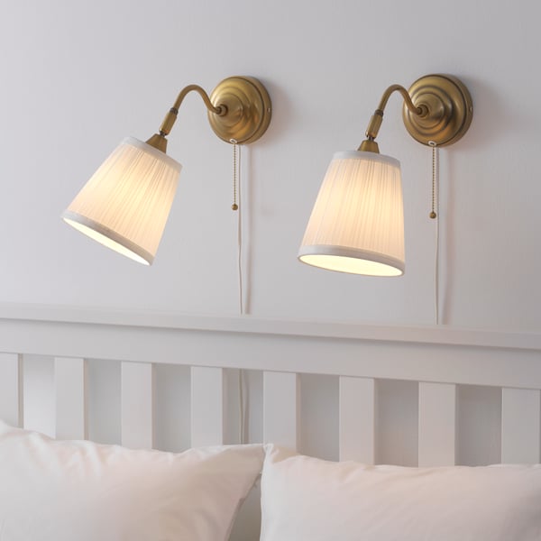 Two IKEA ÅRSTID brass/white wall lamps on top of the bed frame in the bedroom. 