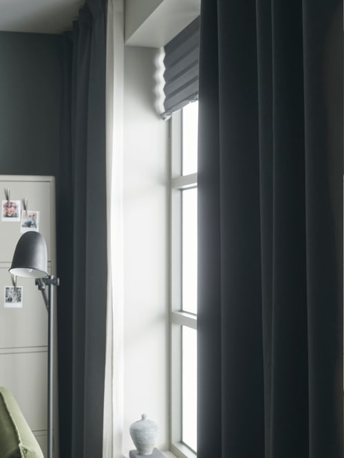 Prim-plan cu o cameră de zi modernă cu stor opac plisat, draperii semiopace și o lampă de citit.