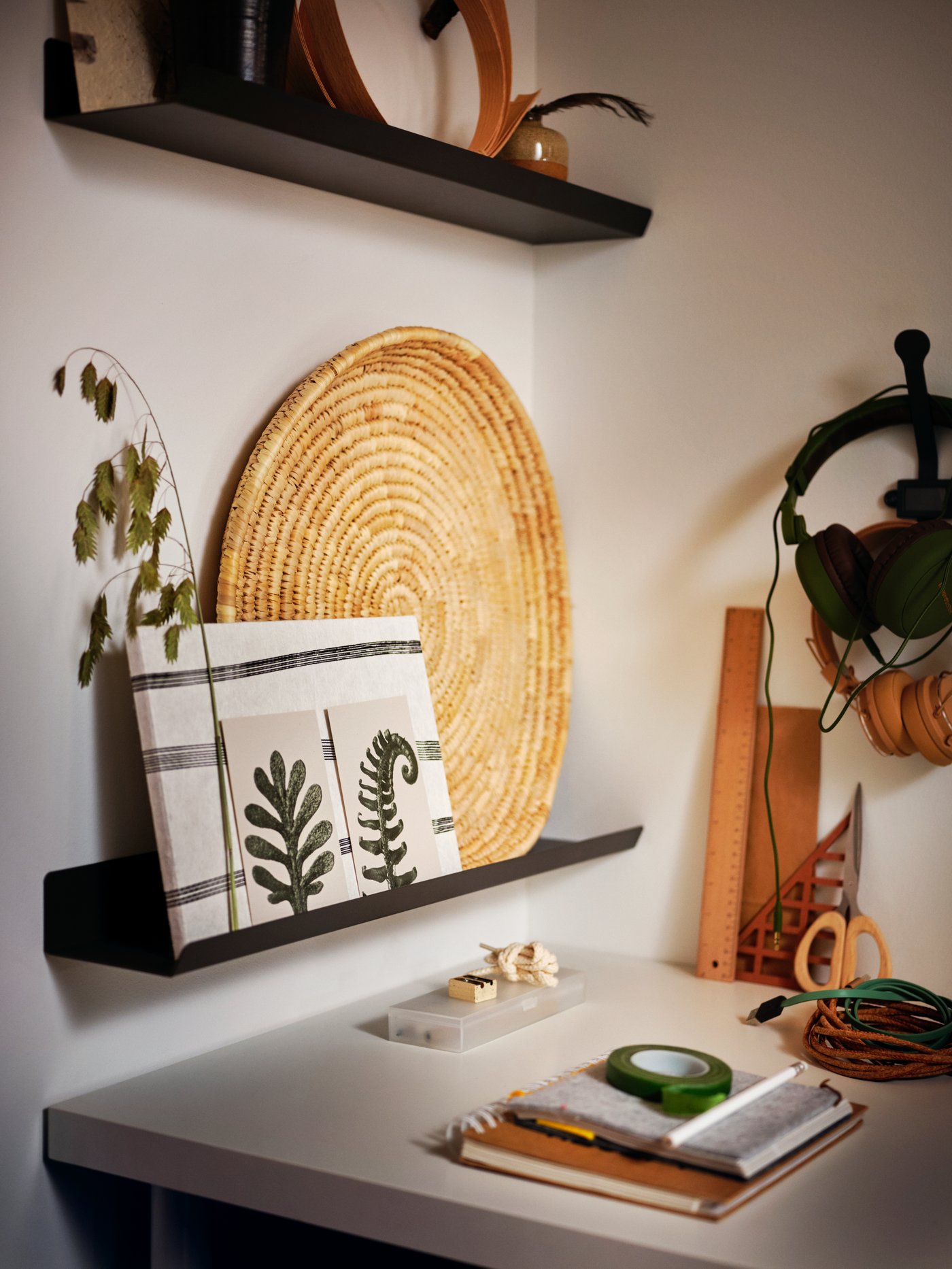 A desk placed into a corner, with decorative objects placed on dark-grey MALMBÄCK display shelves on the wall above.