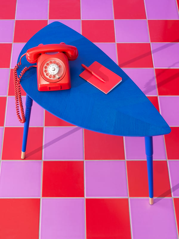 A red retro telephone, notebook and pen are on a blue LÖVBACKEN side table on a red and lilac square tiled floor.