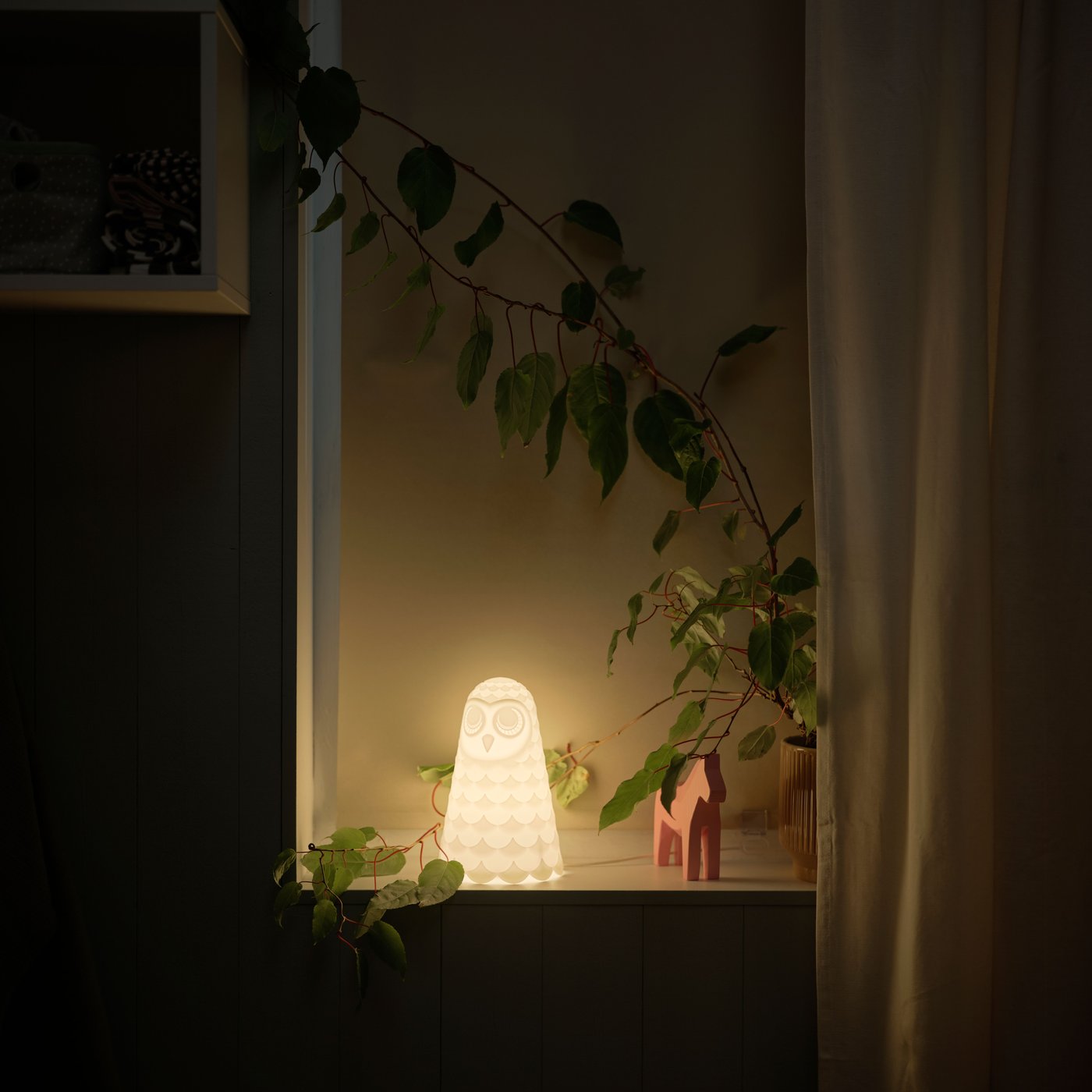 Ett fönster sett inifrån, med en tänd SOLBO LED‑bordslampa formad som en vit uggla i fönstret.

