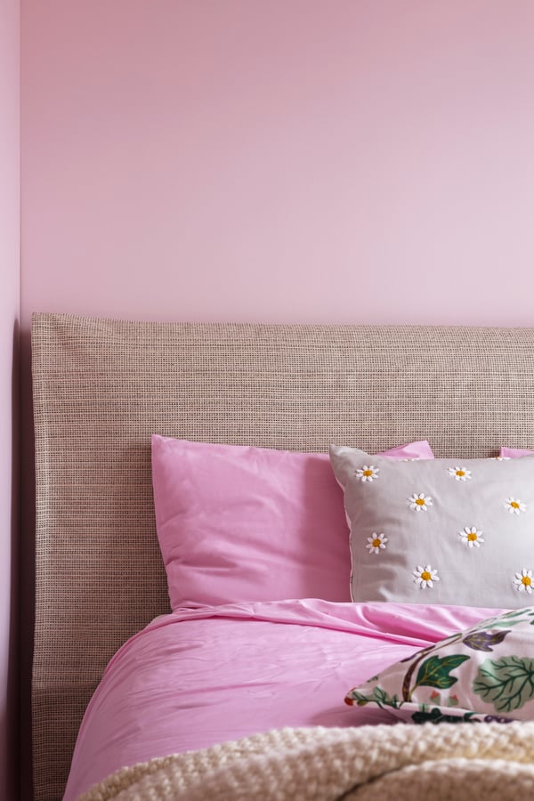 Seng med rosa sengesett. TIPHEDE gulvteppe brukt som trekk til sengegavl.