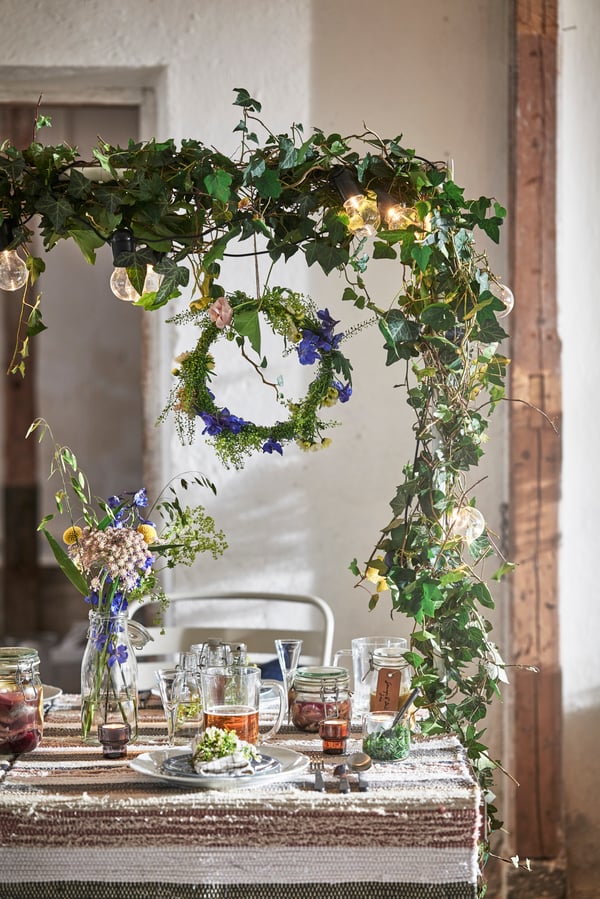Eine festlich gedeckte Tafel mit einem rustikalen Tisch unter einem wunderschönen Bogen aus Efeu und einem hängenden Kranz aus blauen Blumen.