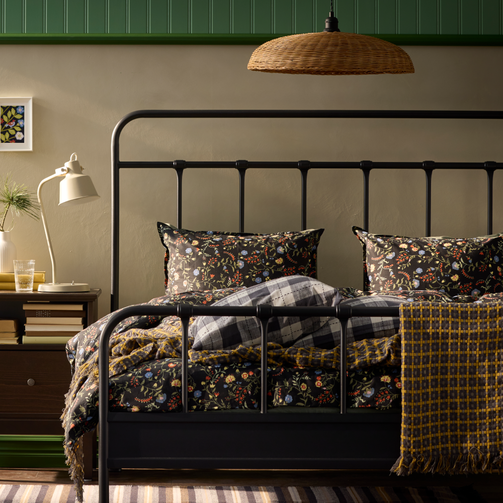 A STJÄRNÖ bed frame with floral bedding stands against a green wall, next to a black bedside table.