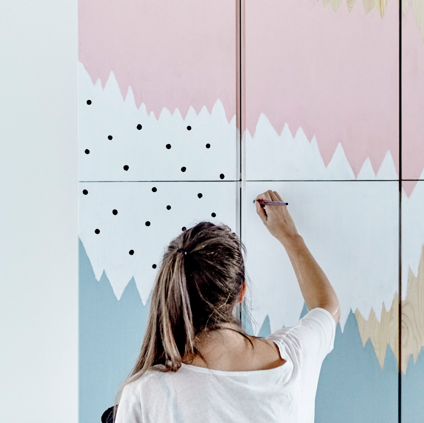 Eine Frau mit langen blonden Haaren mal einen Bild an eine Wand.