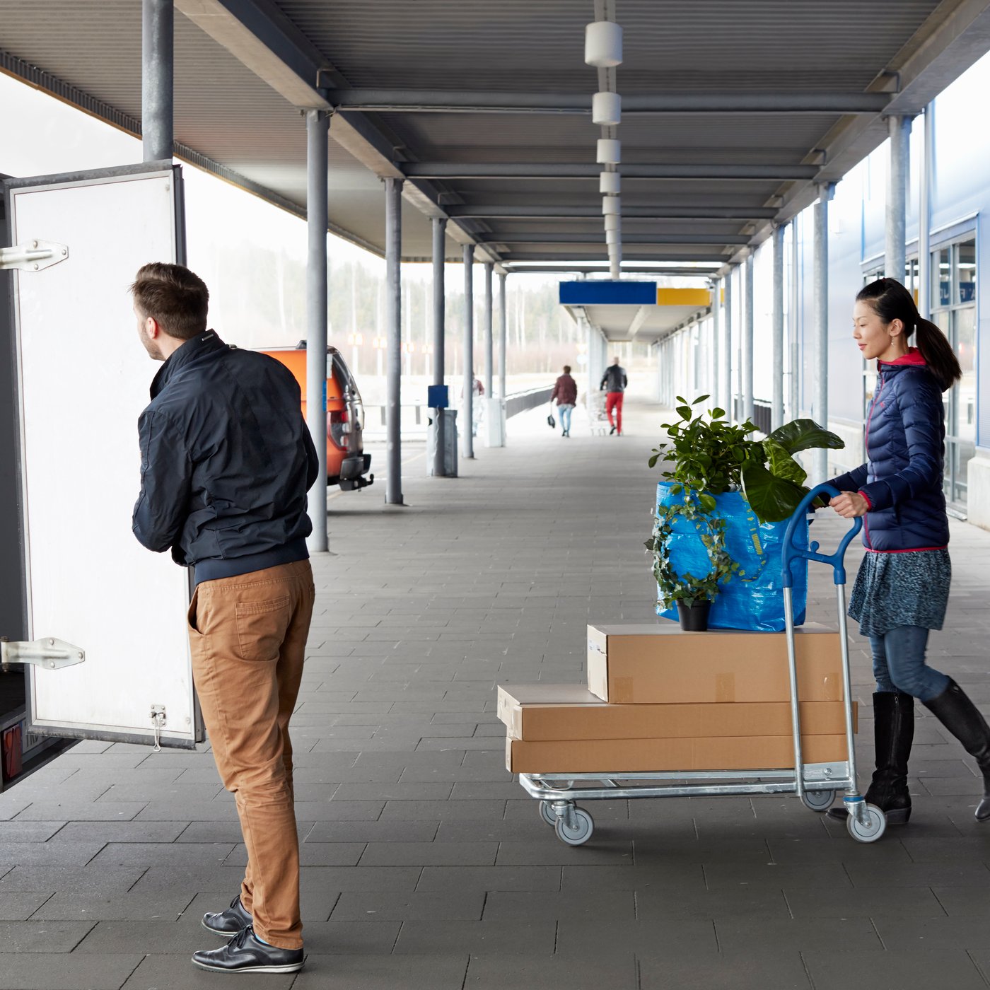 Zwei Personen verlassen mit einem vollen Flachwagen das IKEA Einrichtungshaus und bewegen sich auf einen Mietanhänger zu.
